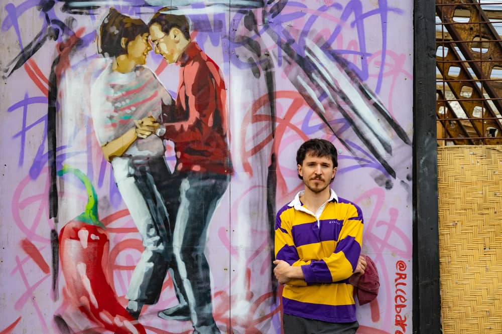 Artist RICE, real name Eduard Sacrest, standing beside a mural